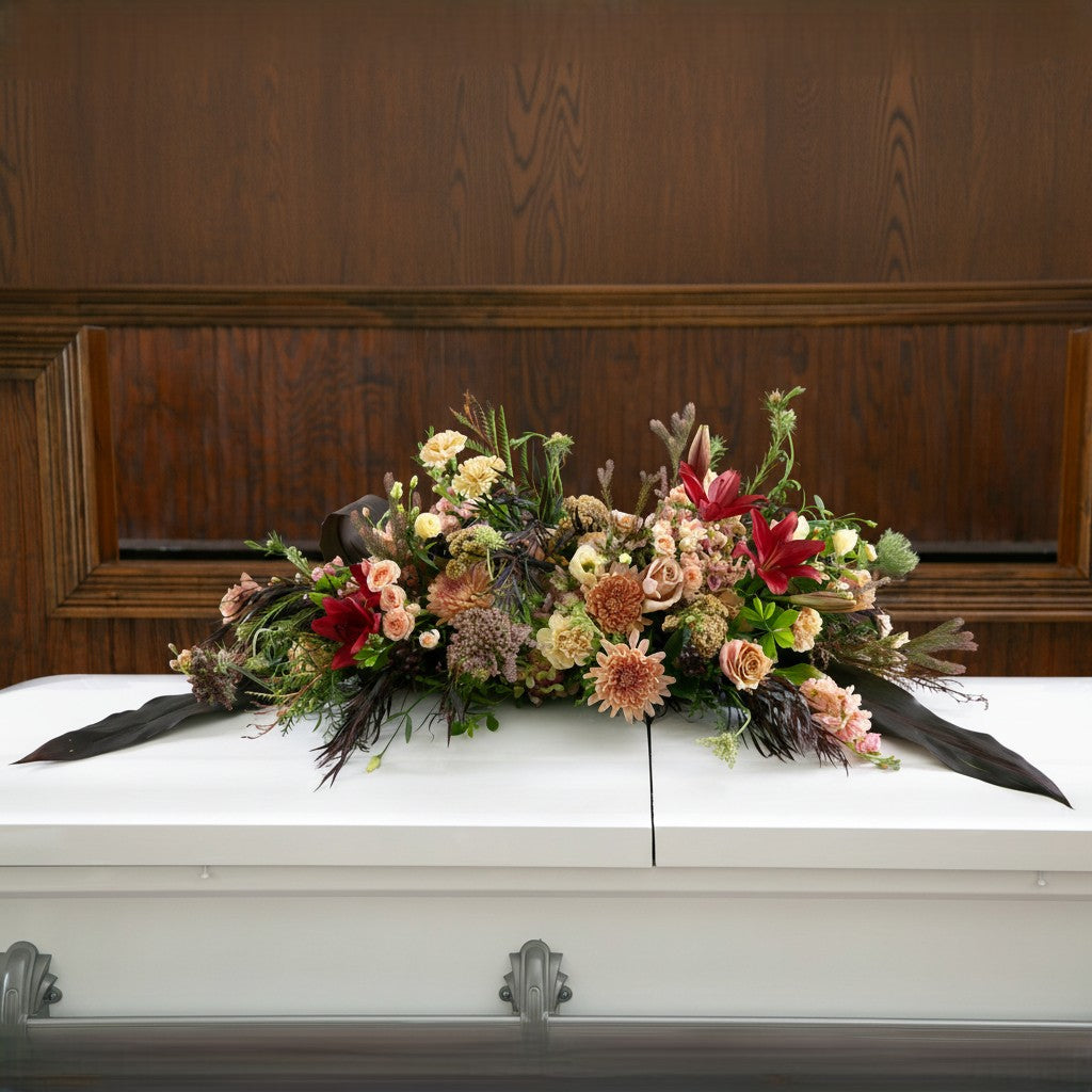 A funeral casket spray with garden style flowers in peach, green, and red