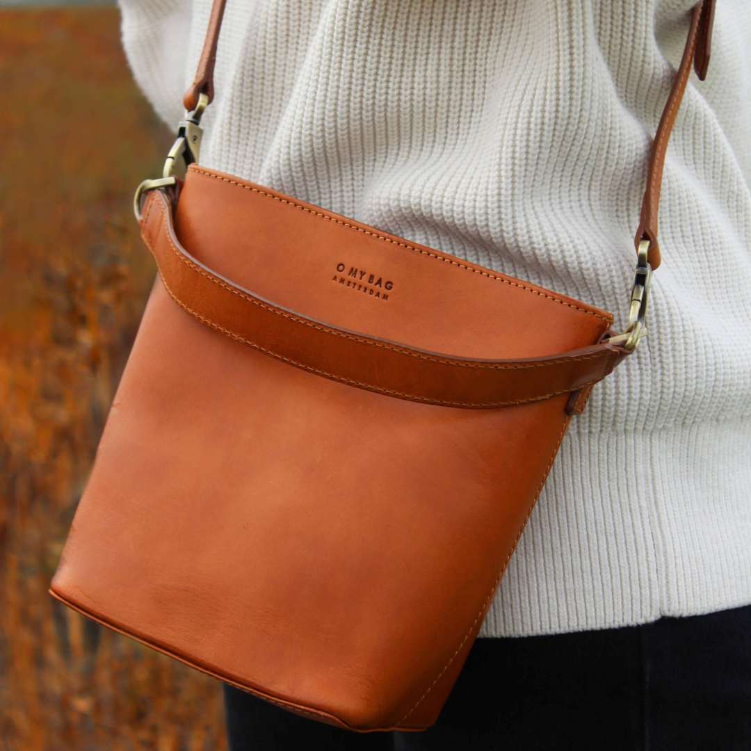 O My Bag Bobby Bucket | Cognac Leather | Brown leather handbag with visible brand name, worn by a person in a white sweater. 