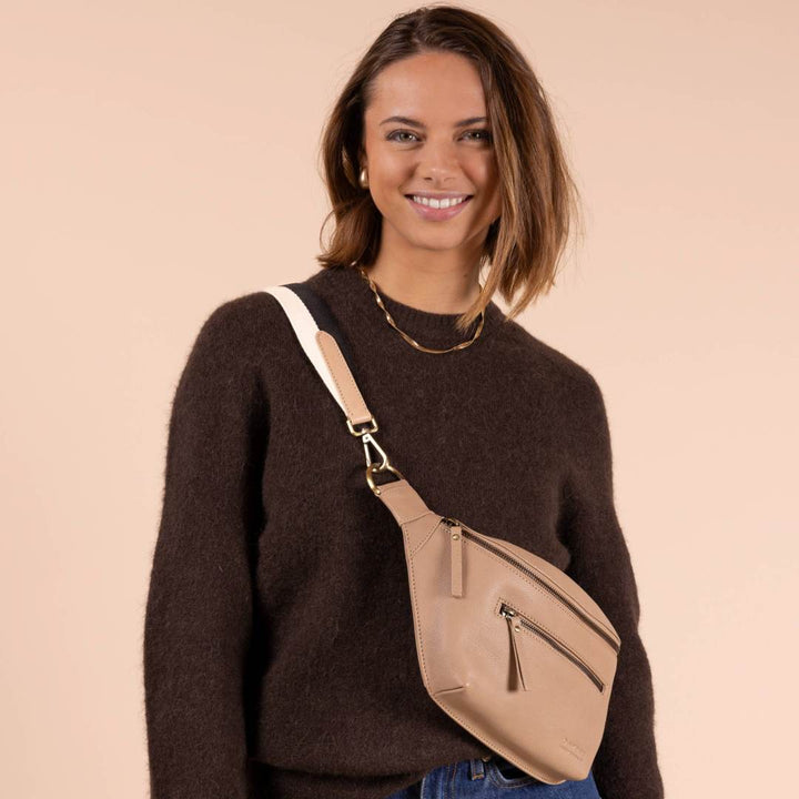 O My Bag | Drew Bum Bag | Woman wearing a brown sweater with a beige crossbody bag on a beige background