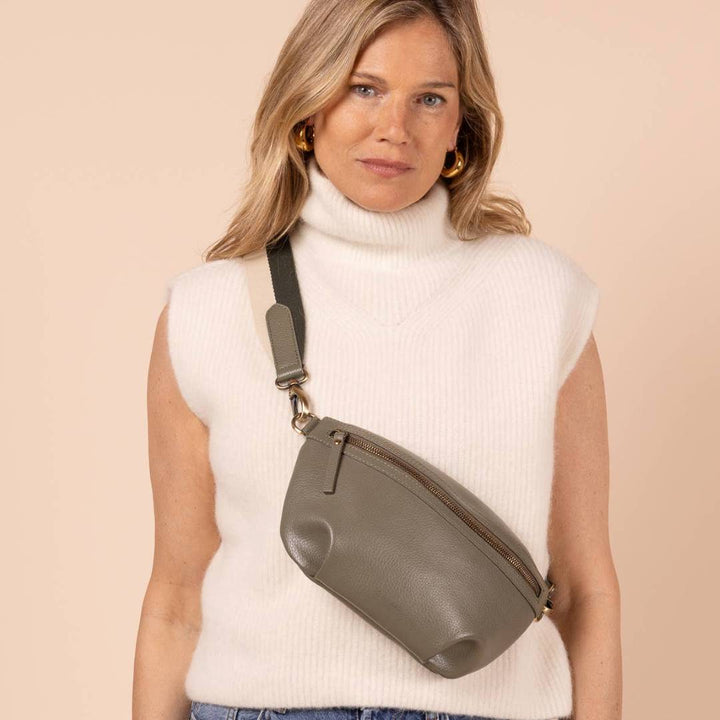 O My Bag | Milo Sage Green Crossbody bag | Woman wearing a white sleeveless top, blue jeans, and a green crossbody bag against a beige background