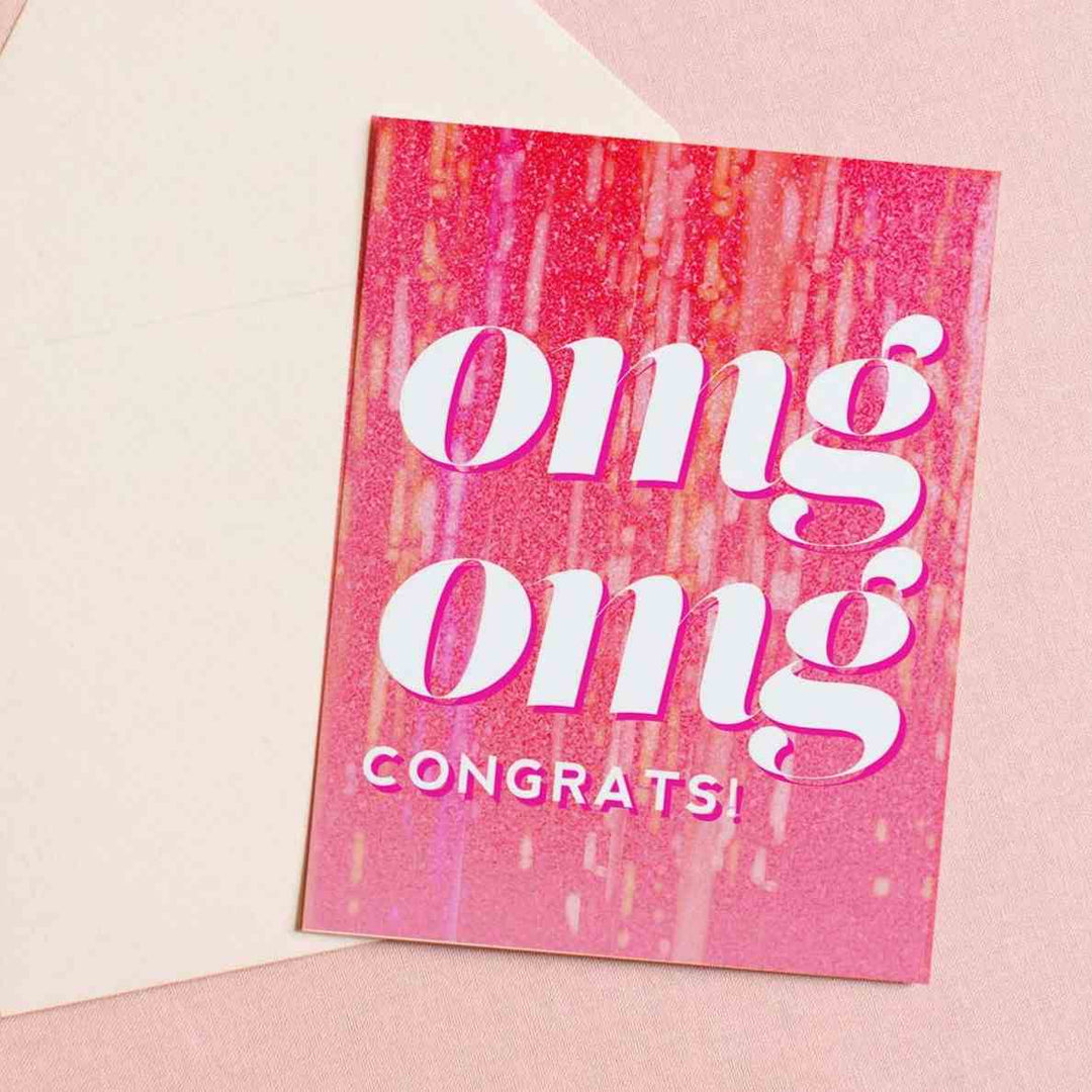 A pink sparkly card with large text that reads "omg omg congrats!" Comes with a cream envelope.