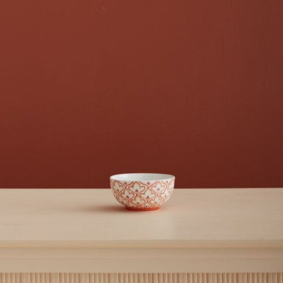 Small ceramic bowl with decorative pattern on a wooden surface and red wall background
