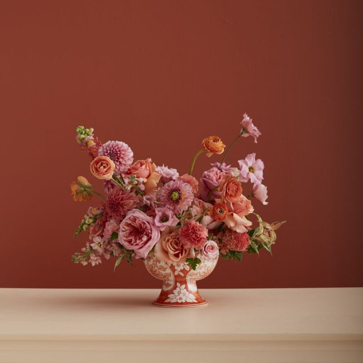 Floral arrangement in a decorative vase against a red-brown background