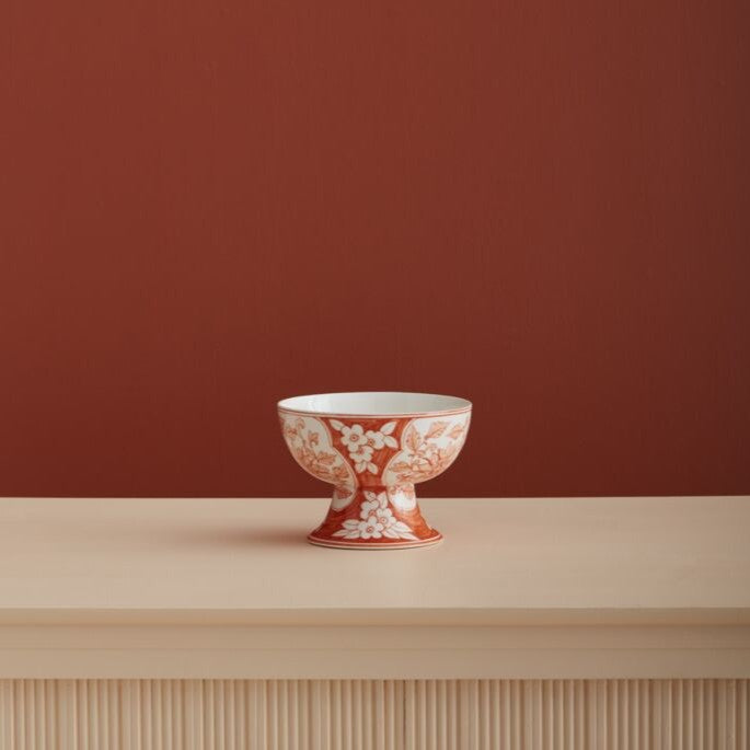 Decorative ceramic bowl with floral pattern on a wooden surface and red wall background