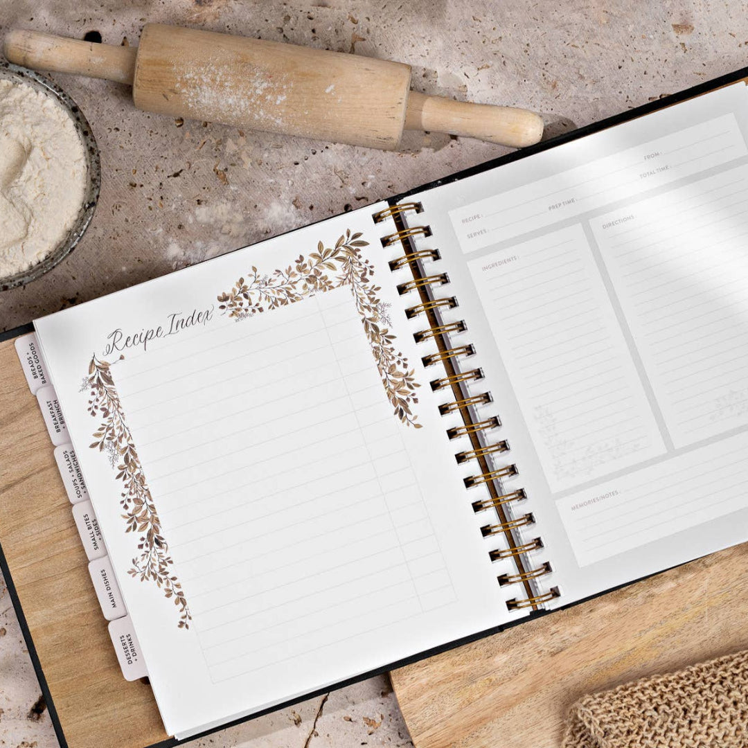 Open planner recipe book with decorative elements on a kitchen counter with flour and rolling pin.