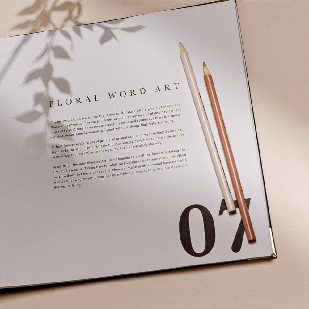 Open book with floral word art and two pencils on a light surface