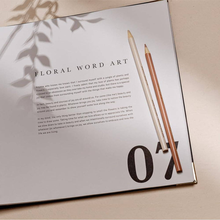 Open book with floral word art and two pencils on a light surface