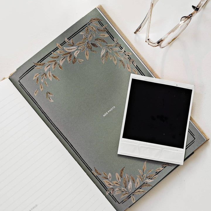 Gray notebook with floral design and a black square photo on a white surface