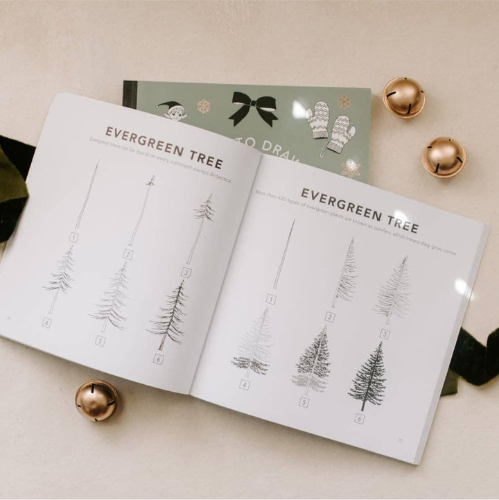 Open book with illustrations of evergreen trees on a light surface with decorative items.