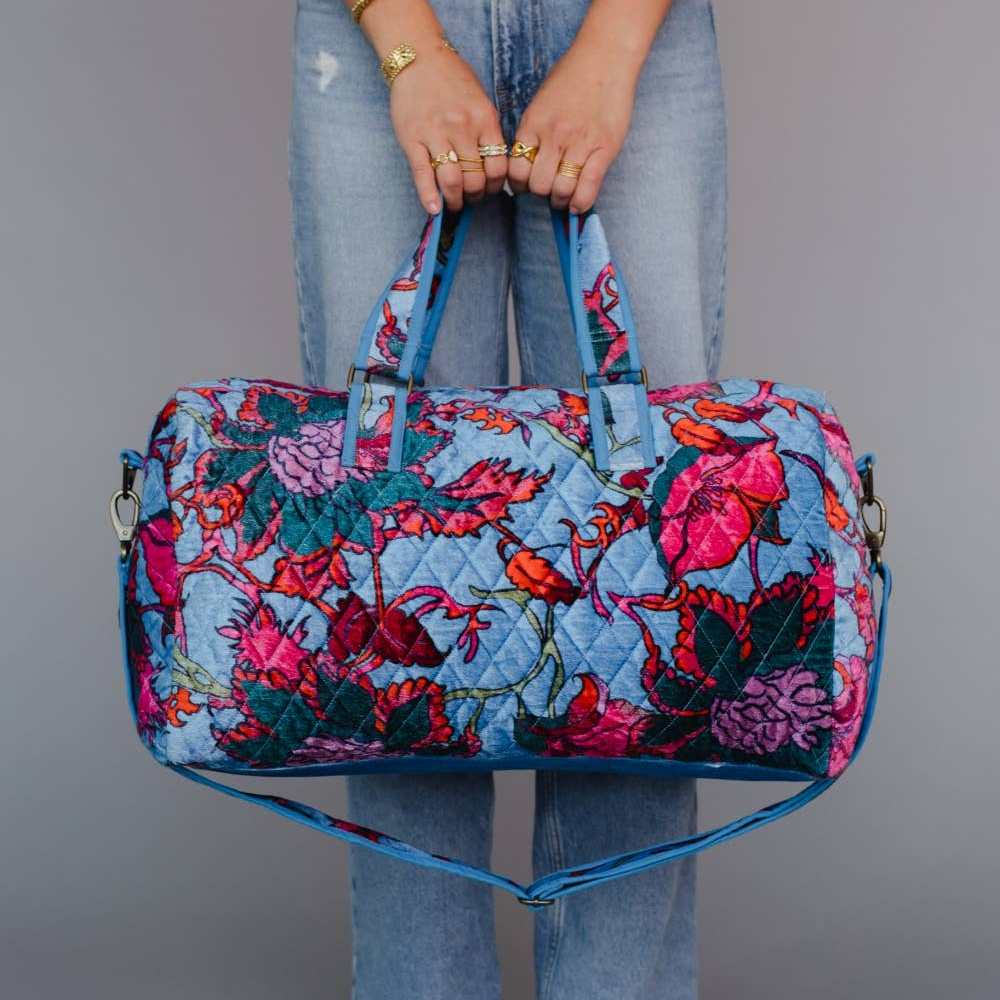 Panache Apparel Co. | Person holding a blue floral duffel bag against a gray background
