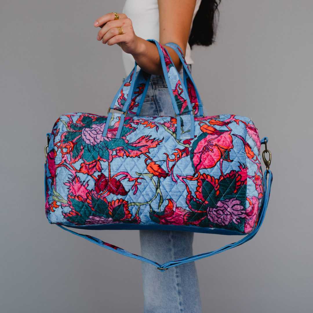 Panache Apparel Co. | Blue floral patterned bag held by a person against a gray background