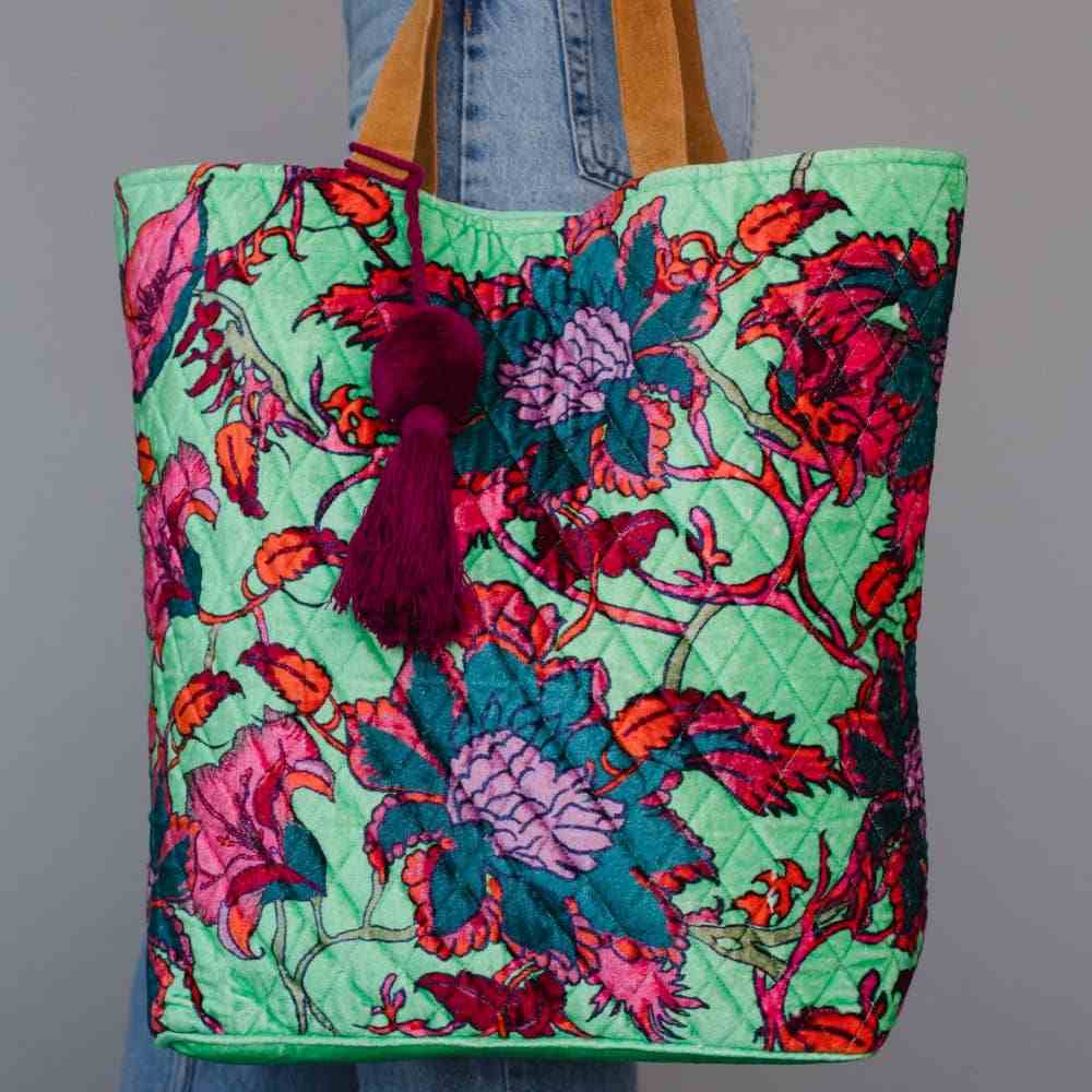 Panache Apparel Co. | Green floral patterned tote bag with tassel held by a person wearing jeans against a gray background