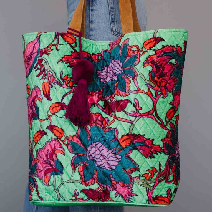 Panache Apparel Co. | Green floral patterned tote bag with tassel held by a person wearing jeans against a gray background