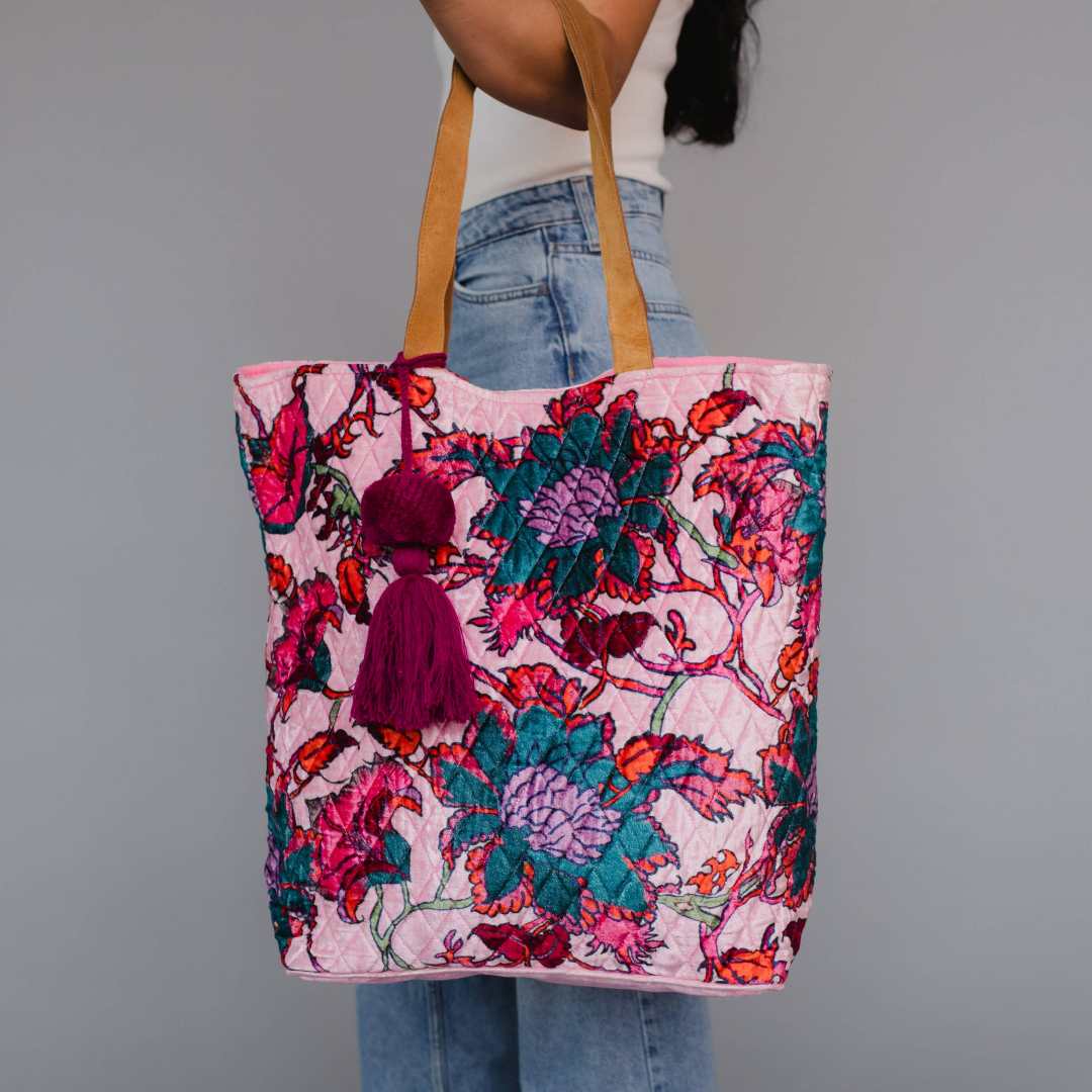 Panache Apparel Co. | Person holding a colorful pink floral tote bag with a tassel on a gray background