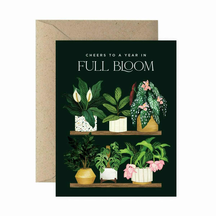 Paper Anchor Co. | Full Bloom Plant Shelf Birthday Greeting Card | A black card with watercolor houseplants in pots on a shelf. Text reads "Cheers to a year in full bloom". Kraft brown envelope included.