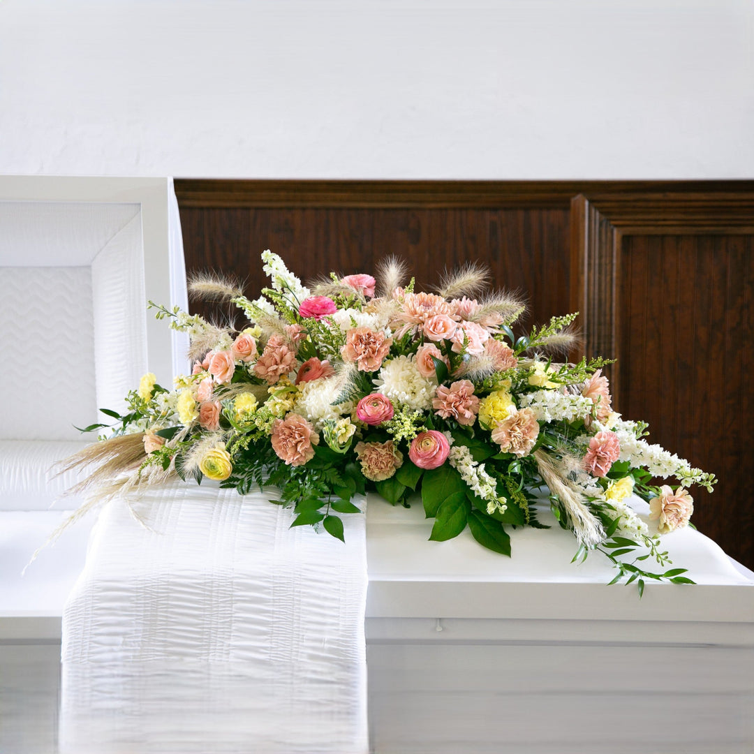 Floral arrangement on a white casket with a wooden background