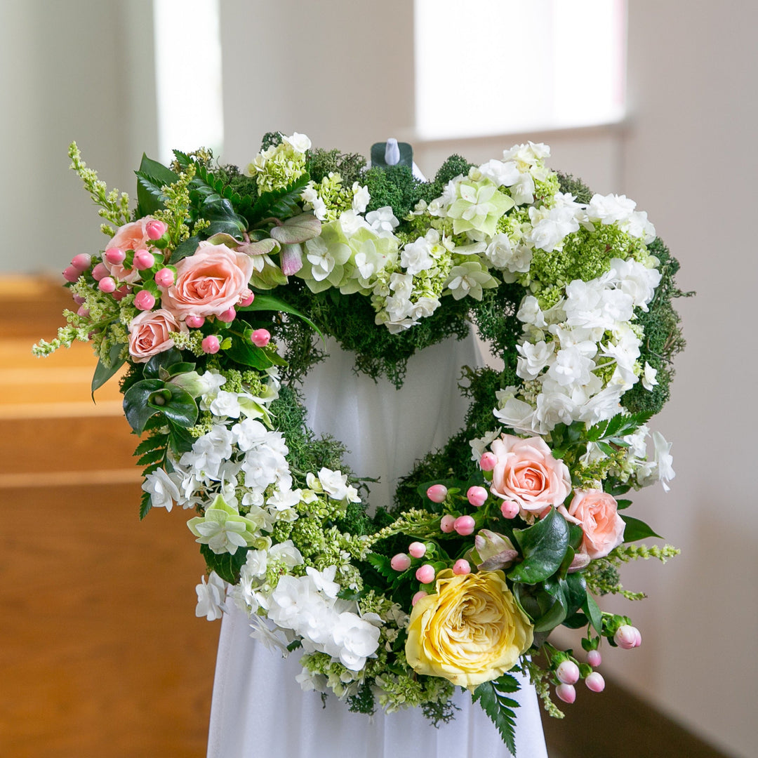 Heart-shaped floral arrangement with white, pink, and yellow flowers on a white background.