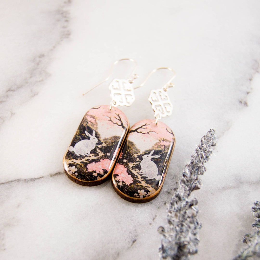 Pair of earrings with rabbit and floral design on a marble surface