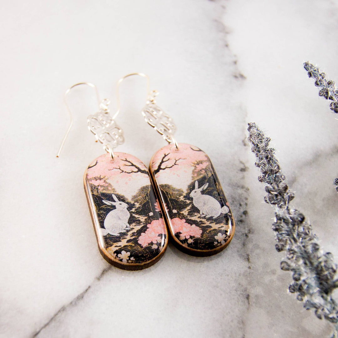 Pair of earrings with rabbit and floral design on a marble surface