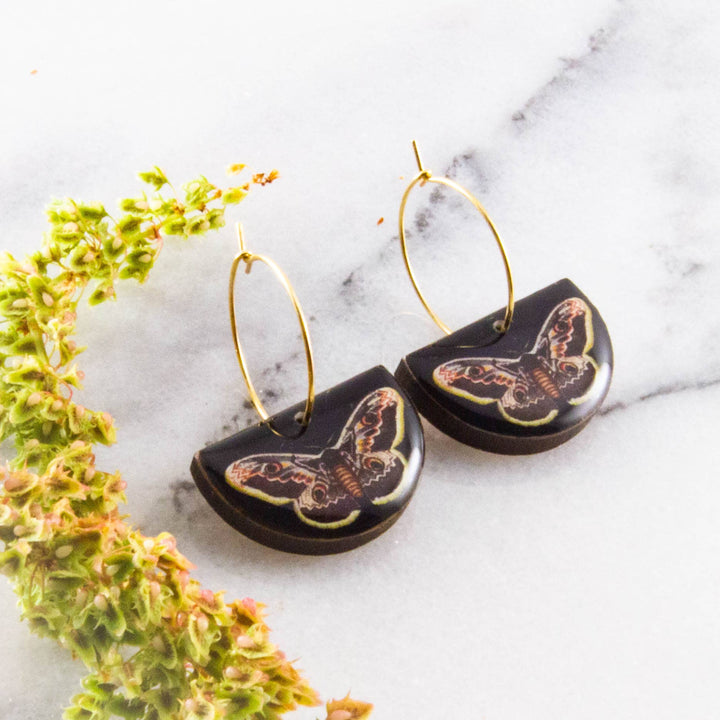 Moth-themed earrings on a marble surface with green leaves.