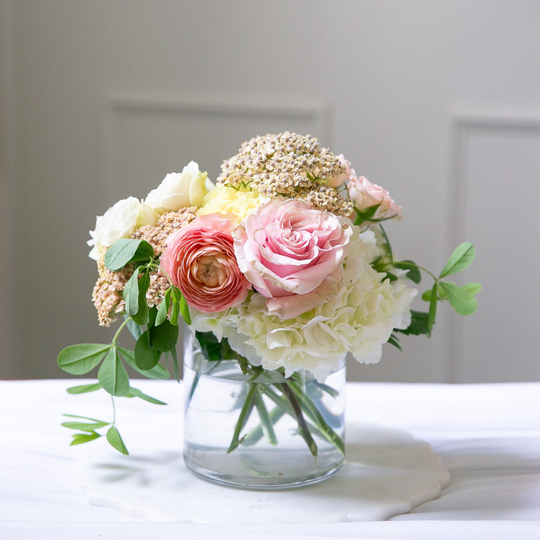 Bouquet of flowers in a clear vase on a white surface with a neutral background