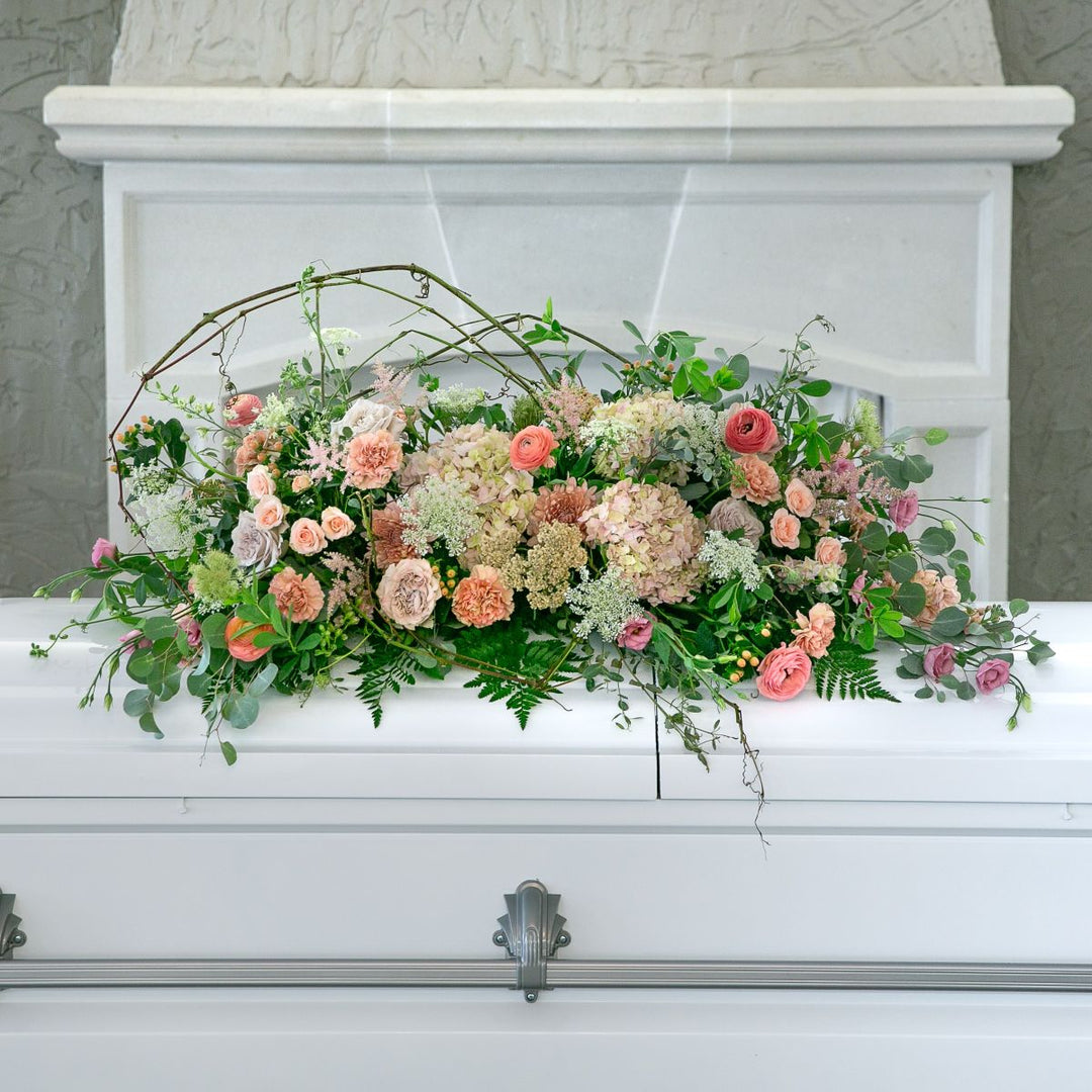 Floral arrangement on a white casket with a marble headboard.