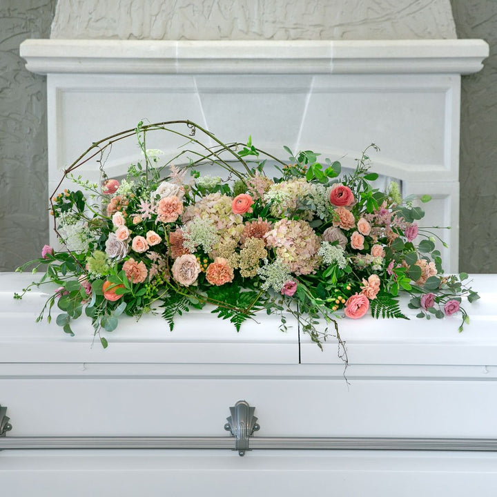 Floral arrangement on a white casket with a marble headboard.
