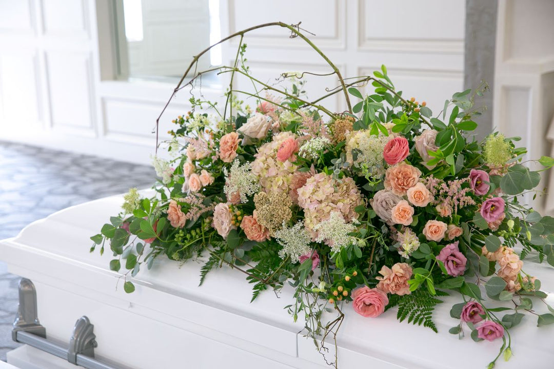 Floral arrangement on a white casket in a room with white walls.
