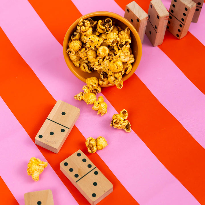 Wooden dominoes with popcorn on a pink and orange striped background