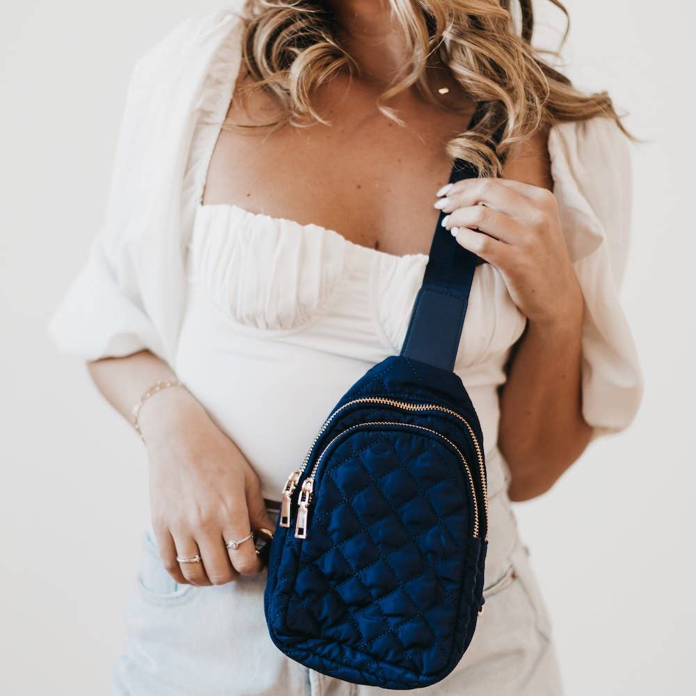 A model holding a navy blue crossbody bag with gold hardware.