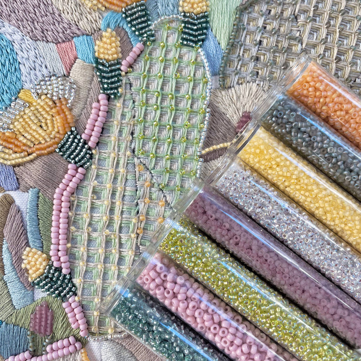 Close-up of embroidered fabric with colorful beads and packaging of beads.