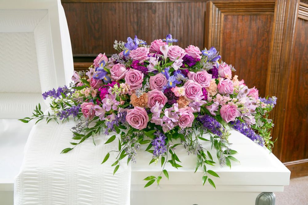 Colorful floral arrangement on a white casket in a funeral setting.