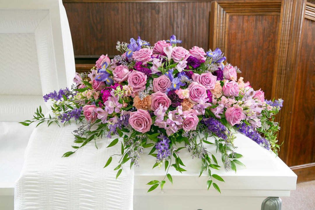 Colorful floral arrangement on a white casket in a funeral setting.