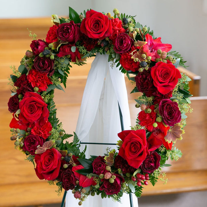 Floral wreath with red and pink roses on a white stand against a wooden background