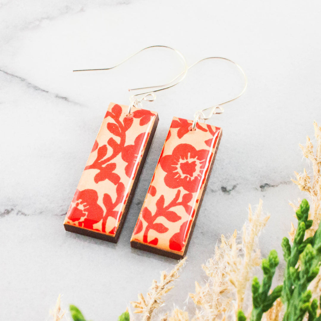 Pair of red floral earrings on a marble surface with plants.