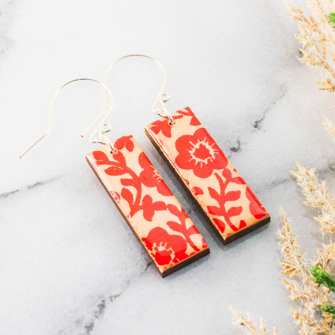 Red floral patterned earrings on a marble surface with dried plants.