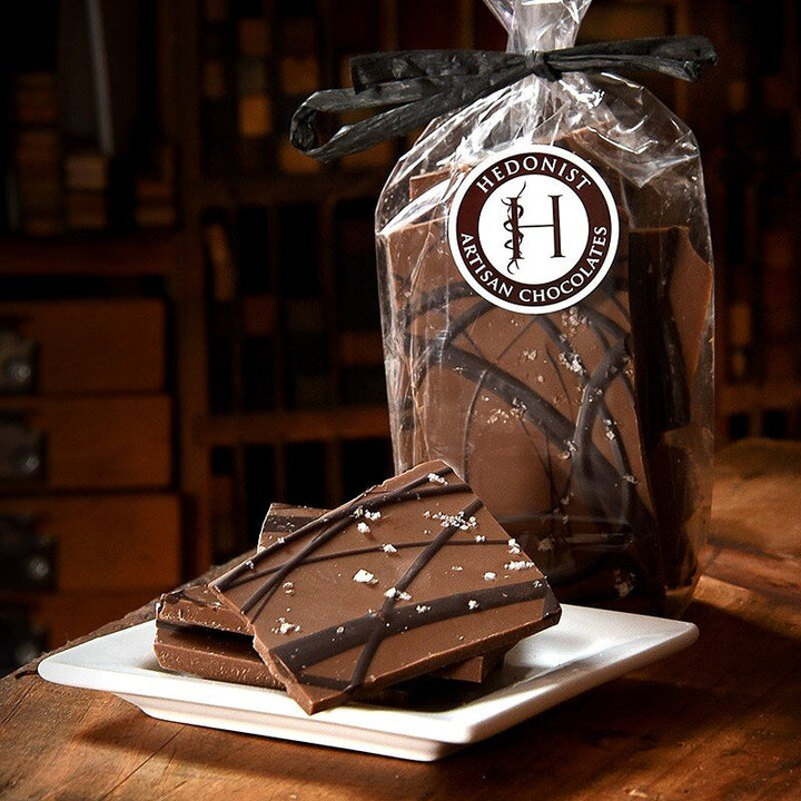 Hedonist Chocolate Bark | Salted Milk Chocolate with Dark Chocolate swirl. Bark displayed on a white plate and in a clear bag tied with a black bow.