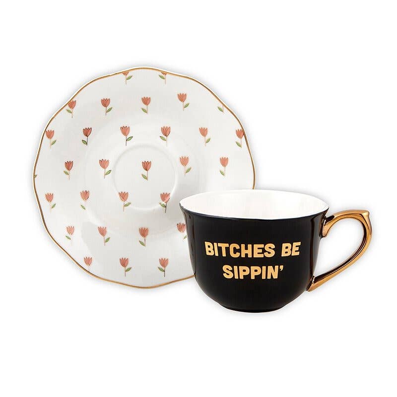 Slant | Black teacup with gold accents and text "Bitches Be Sippin" with a white saucer accented with tiny florals.