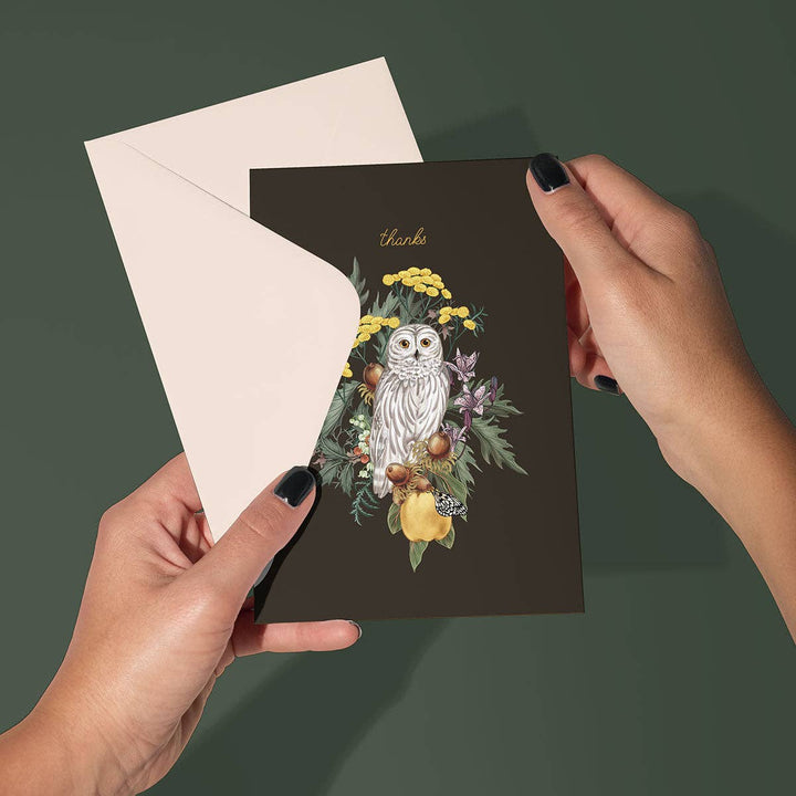 Card with owl and floral design held by hands against a dark green background