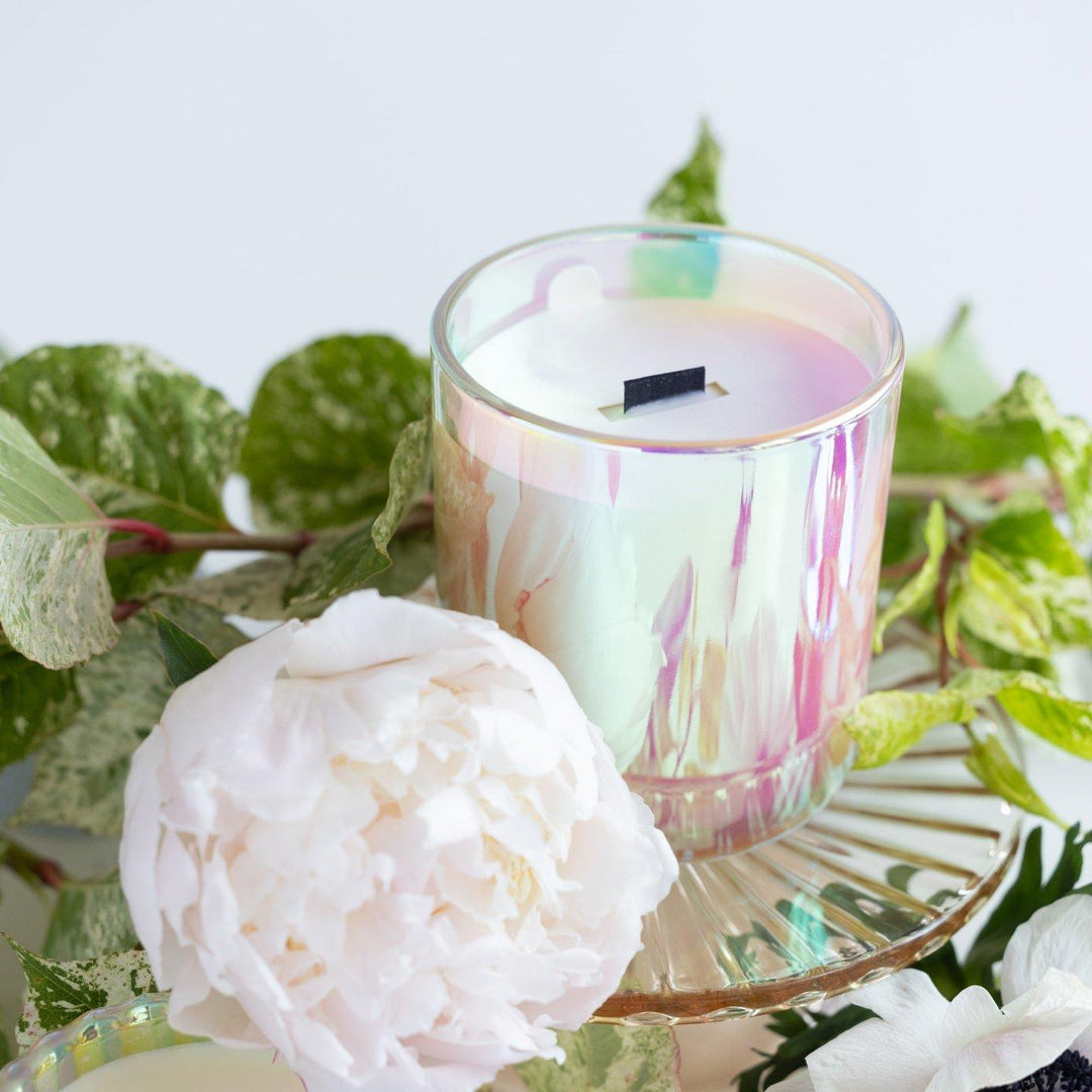 Iridescent candle with black wood wick in Stacy K's signature scent close up with blooms. 