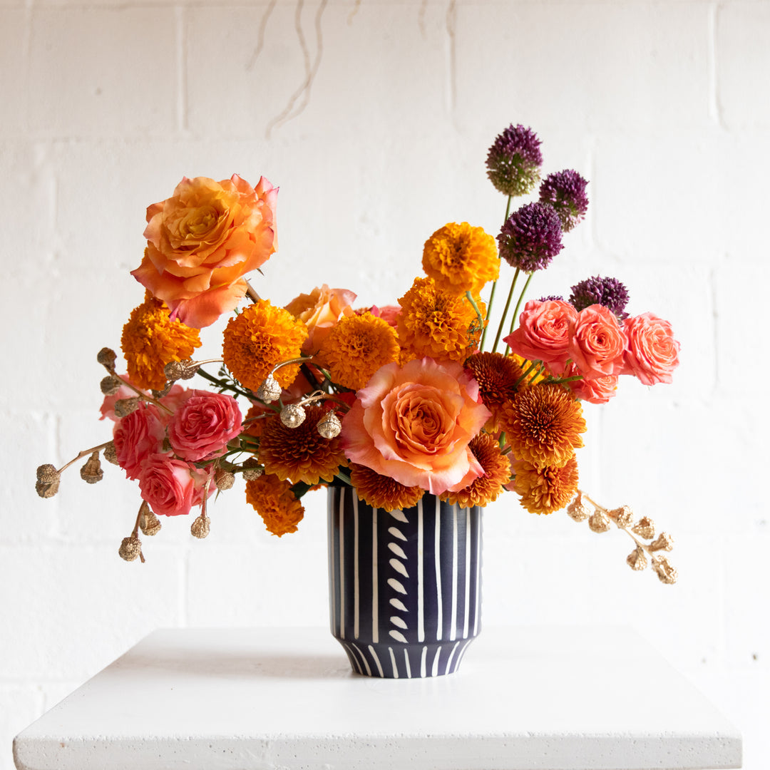 Colorful flower arrangement in a black and white vase on a white surface with a light gray background