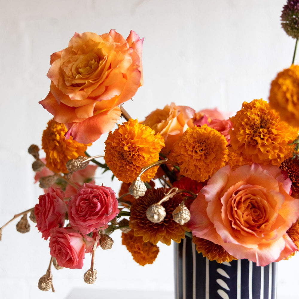 Bouquet of flowers including roses and marigolds in a vase on a white background