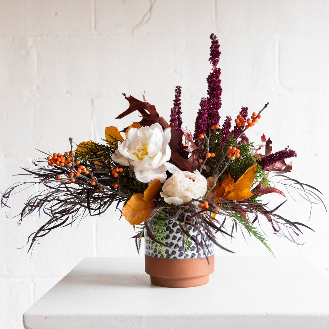 Autumnal floral arrangement in a terracotta pot on a white surface with a white background