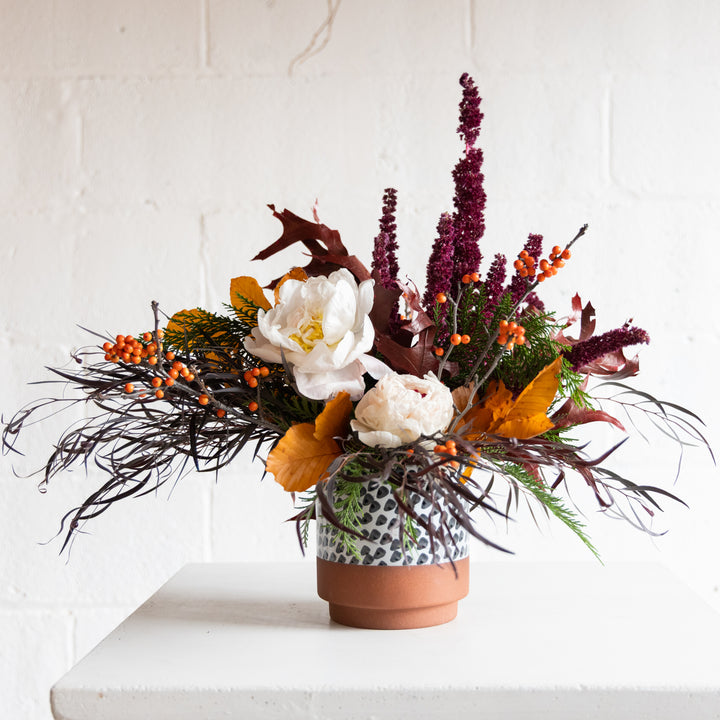Autumnal floral arrangement in a terracotta pot on a white surface with a white background