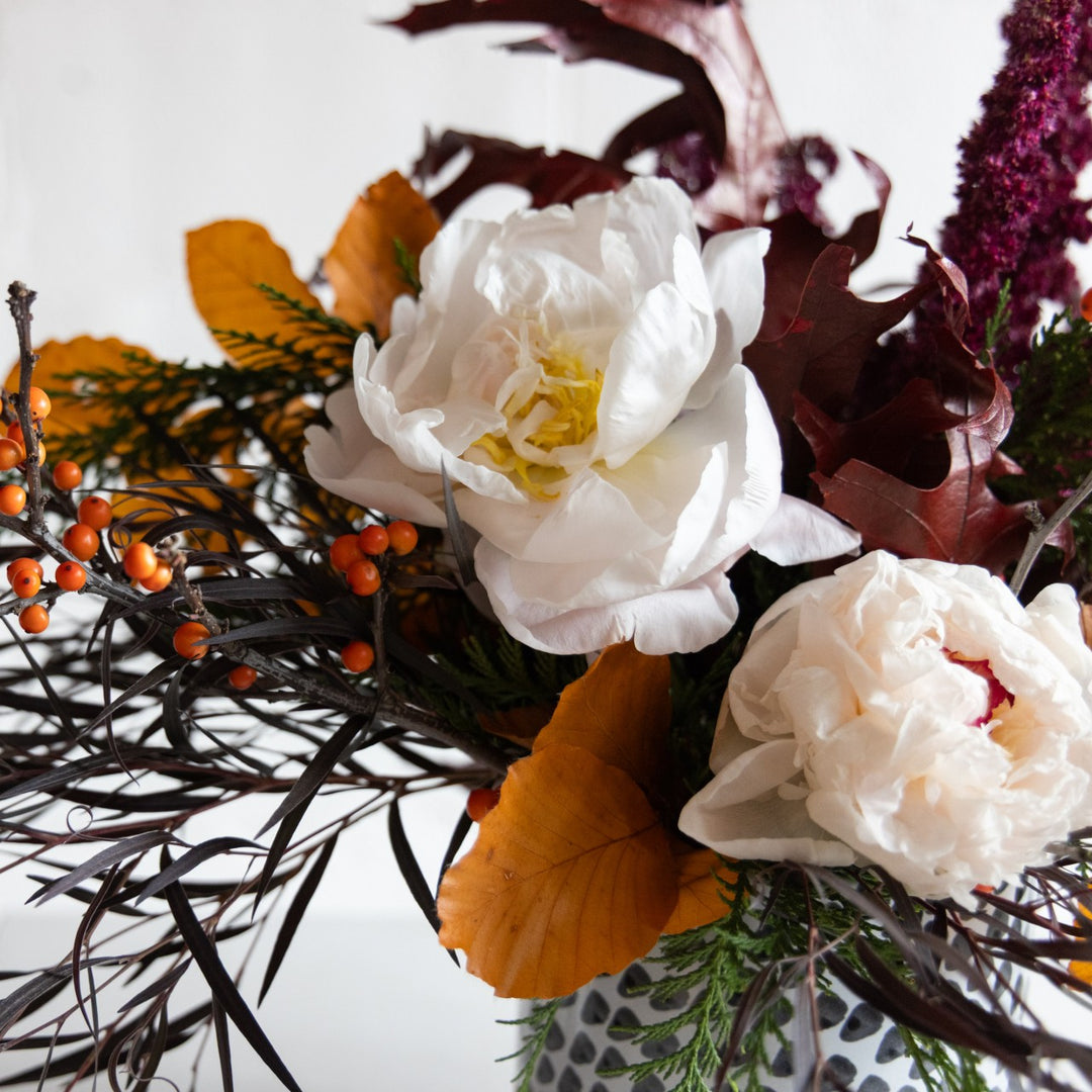 Close-up of a floral arrangement with white flowers, orange leaves, and berries on a white background