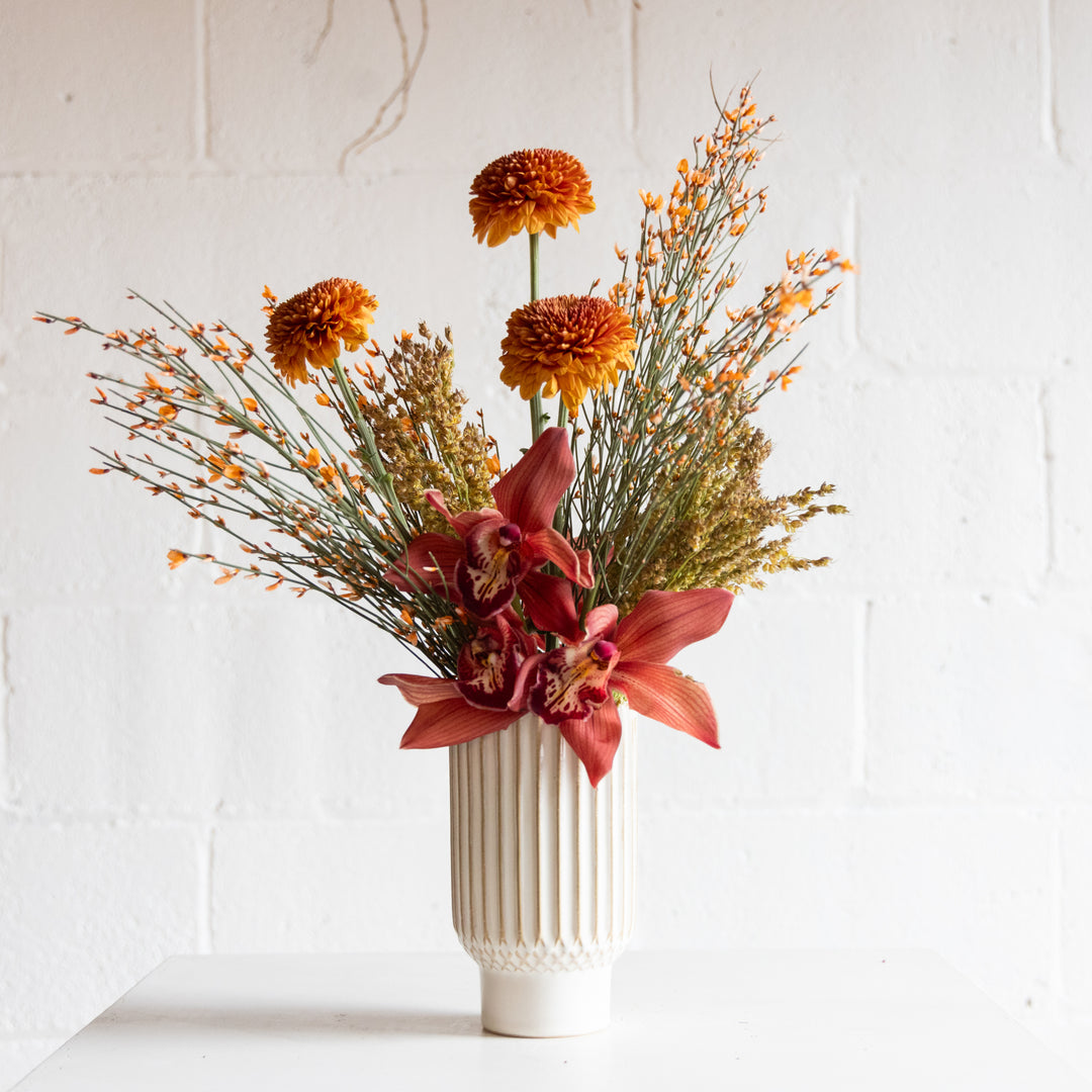 Floral arrangement with orange and pink flowers in a white vase on a light background