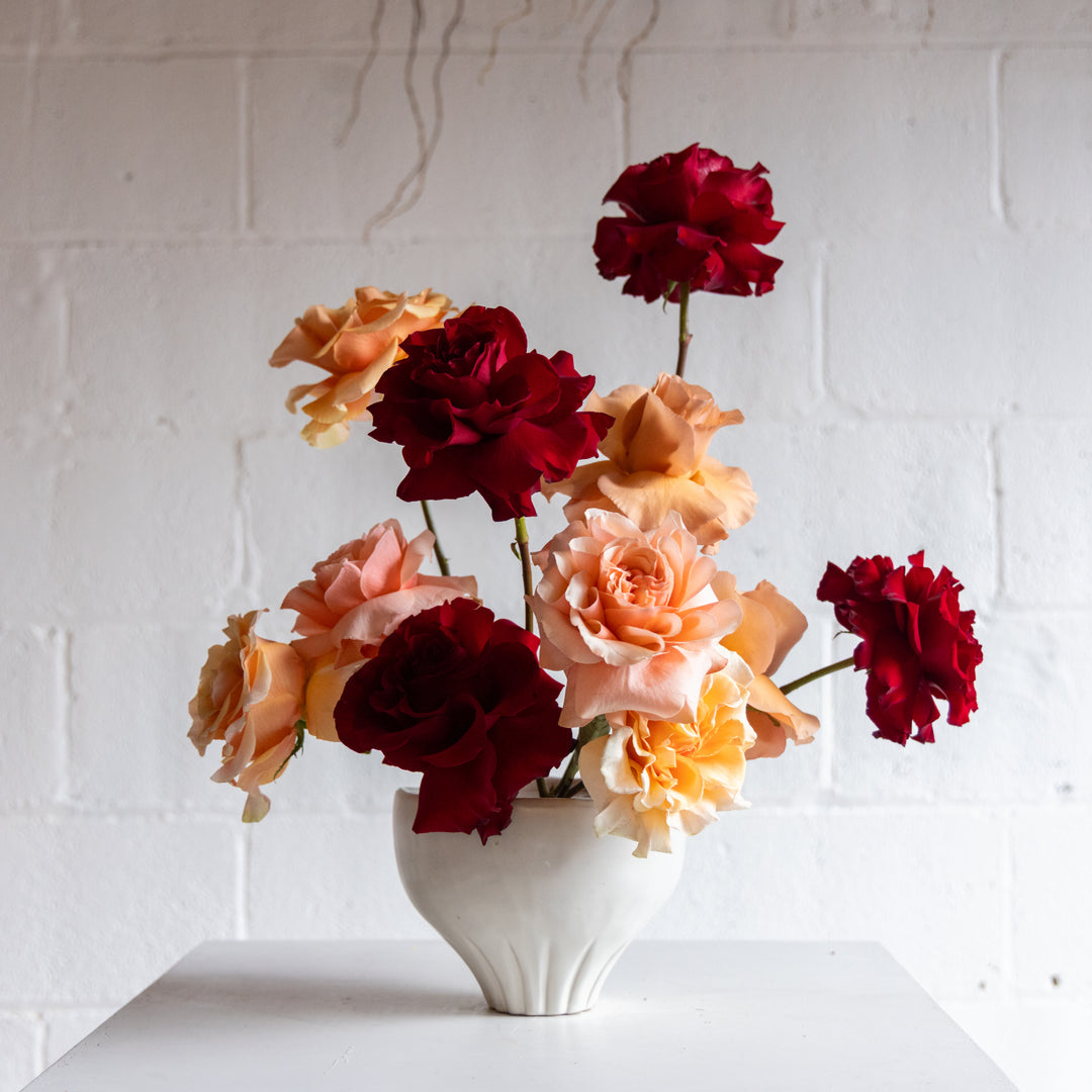Vase with red and peach flowers against a white brick wall