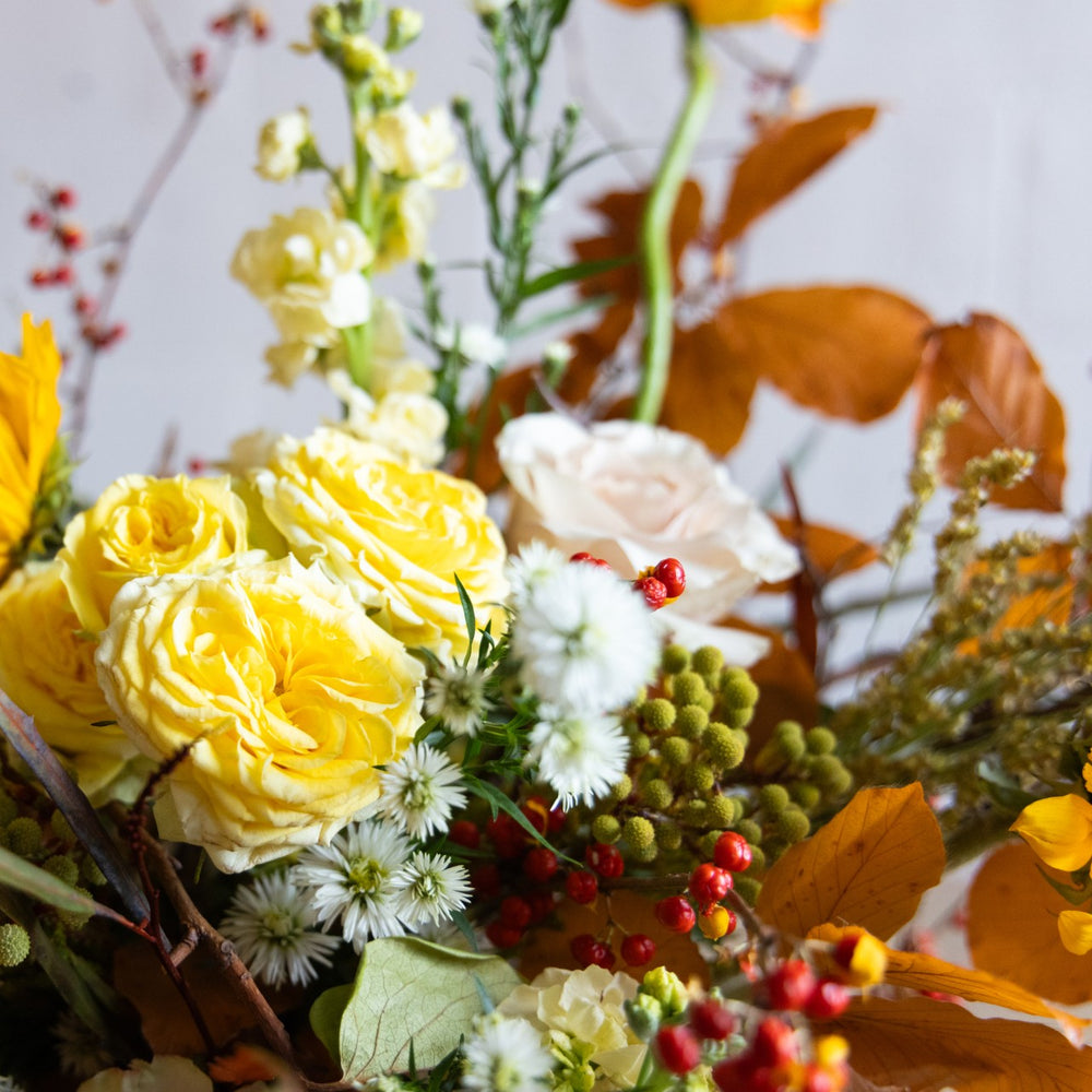 Bouquet of yellow and white flowers with greenery and berries on a light background
