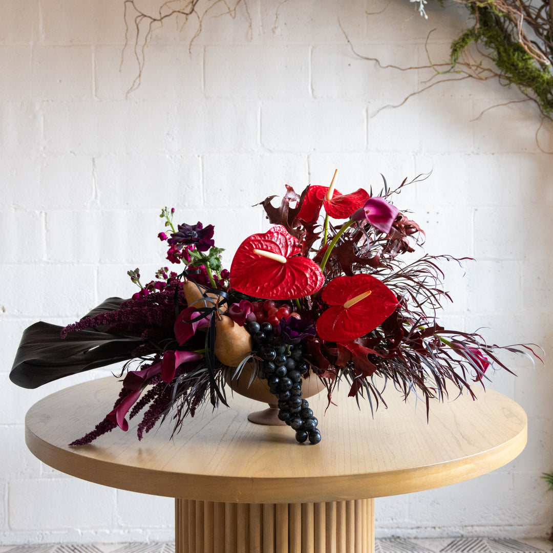 Bouquet of red flowers and dark green leaves on a wooden table with a white brick wall background