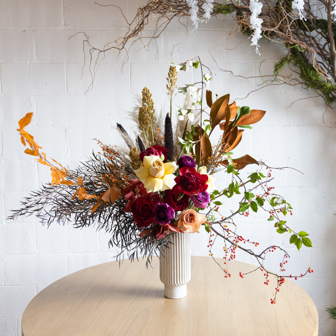 Colorful floral arrangement in a white vase on a light surface with a white tiled wall background.